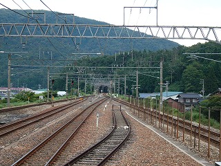 2本に集約される構内の4線。すぐ向こうに低い支尾根をくぐる短いトンネル。背景には山