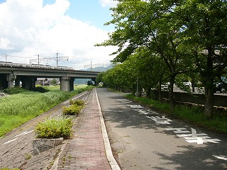 左は草むした掘り込みの川、右は細い道と並木、向こうに湖西線が斜めに跨ぎ、ずっと向こうに山並み。