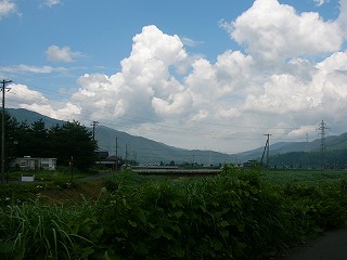 濃い青空、もくもくの厚い雲、山並み、川、とにかく繁茂する草草、向こうに少しの家並み。