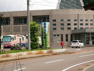 緑と水色の直方体の看板。背景は体育館のような建物。