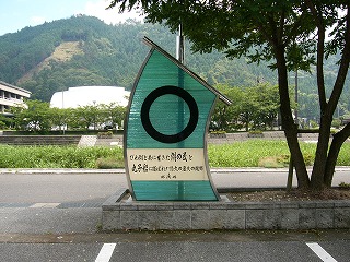 ステンレスで象った帆に横縞の入った水色のガラスを嵌め、そのガラスに太い黒丸を描いたオブジェ。