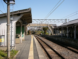 左手に簡単な待合室、右手に線路内を挟んで駅舎。
