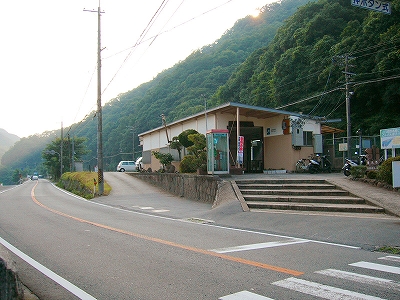 左に伸び行く山間の国道、右手には平たい階段を上った先にある四角い平屋の駅舎。背景はすぐに迫ってきている山。