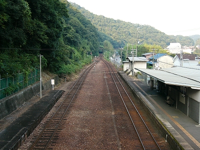 左にこんもりした山肌の緑、焦げ茶のバラストのある広い停車場、右に駅舎の屋根。