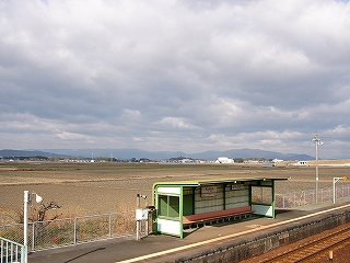 上り線ホームの簡易な待合所とその後ろに広がる冬の田畑。
