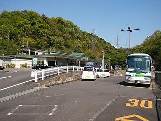 やや起伏のあるロータリー。バス、自動車が停まる。奥のほうは山の緑。