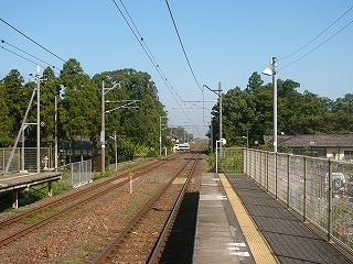 ホームの屋根のなくなったところから、ホームと茶色のバラスとの線路内が青空の下に延びゆくのを眺めて。ホームの終わった少し先には線路の両脇に小さな森がある。