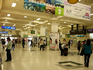 白いタイル床の広いコンコース。たくさんの人が行き交っている。