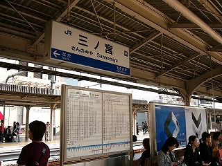 上屋からの駅名ひょう、ホームに立つ時刻表、広告、椅子。