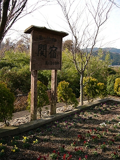 花の咲いた花壇とその背後に立つ「関宿」の木の看板。