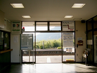 開かれたサッシの引き戸の向こうに、線路を挟んだ向こうにある下り線ホームが見える。下り線ホームの少し奥はたくさんの緑が茂っている。