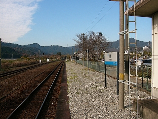 灰色の工事用の砕石で仮舗装されたようなホーム。ずっと遠くには山並み。