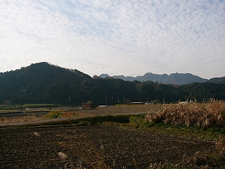 手前から休んだ田んぼが広がる。少し遠くに山が迫ってきてその広がりも途切れている。