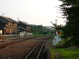 真中が幅広く開いた2線が真近にカーブして消えている。左には真新しいコンクリートの土台の家が2件見えている。