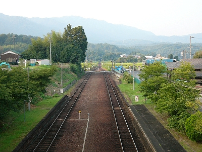 少し遠くで2線が1線になっている。ずっと遠くには県境の大きな山がうっすらと見えている。近くは緑が多い。