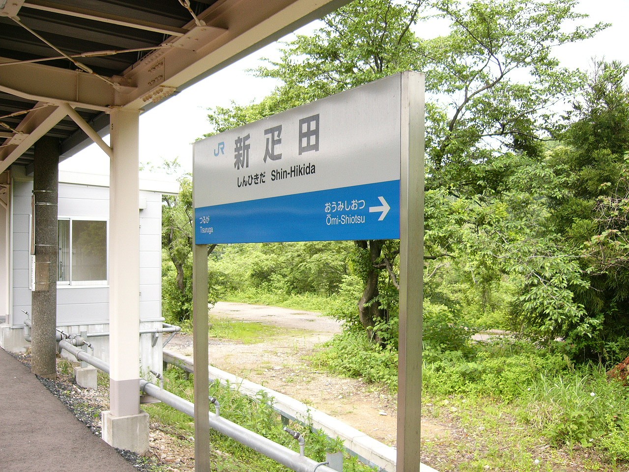 背の高い駅名標と後ろの小径とすぐ上にホームの屋根