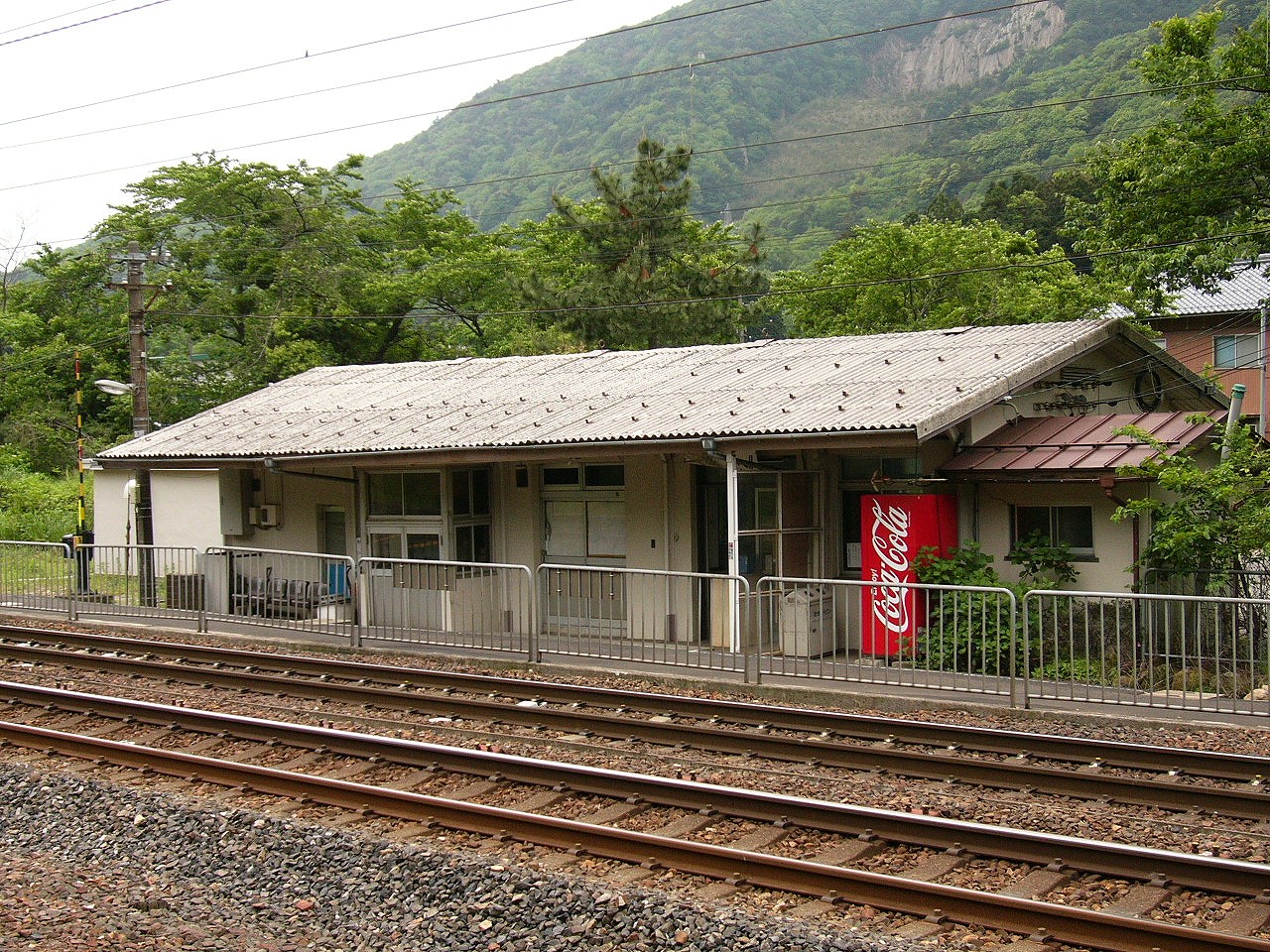 古いコンクリート作りの平屋の駅舎の裏側(構内側)。後ろには山。