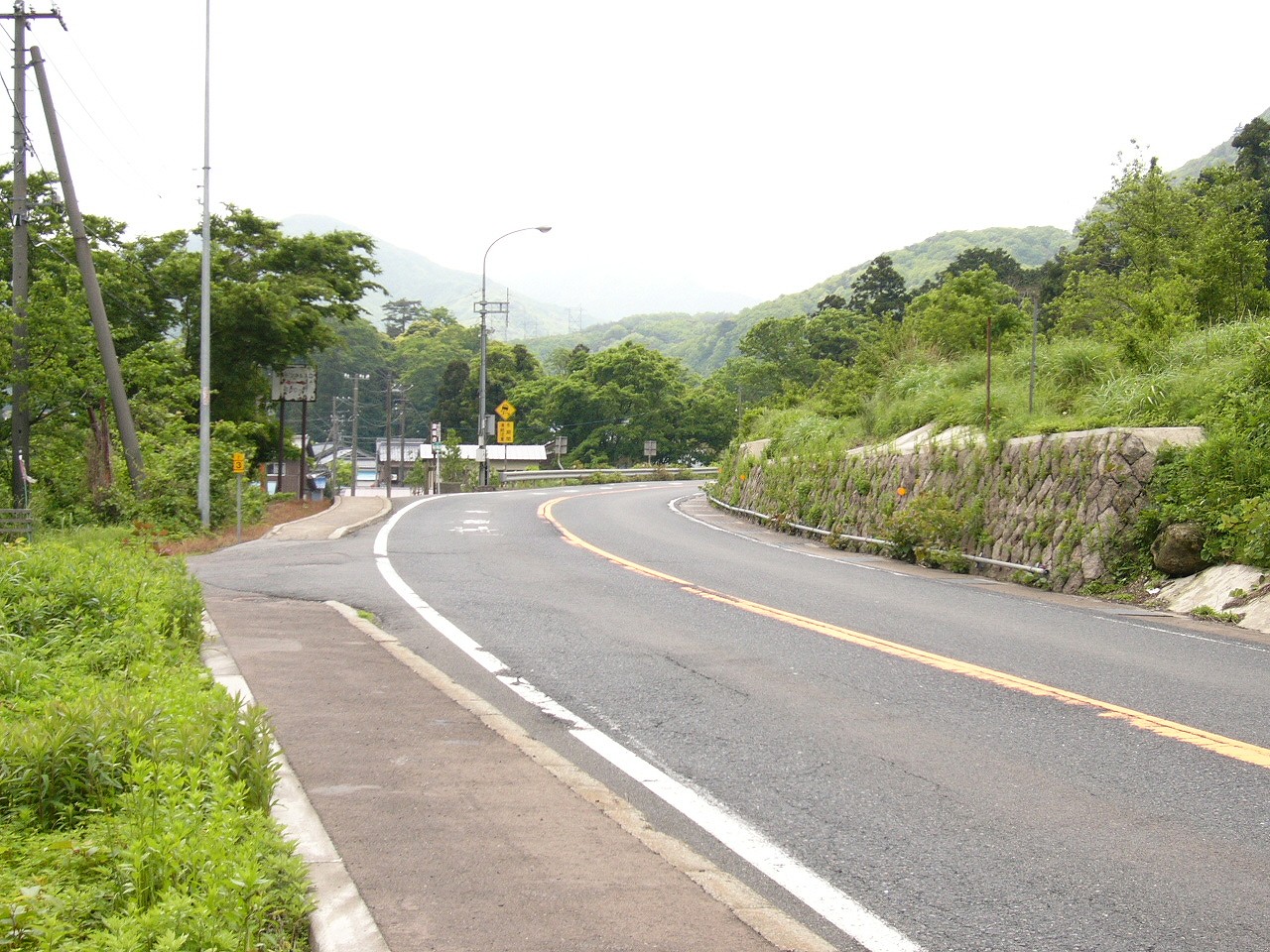 山中の道路カーブ、左手に集落へ下る細道。