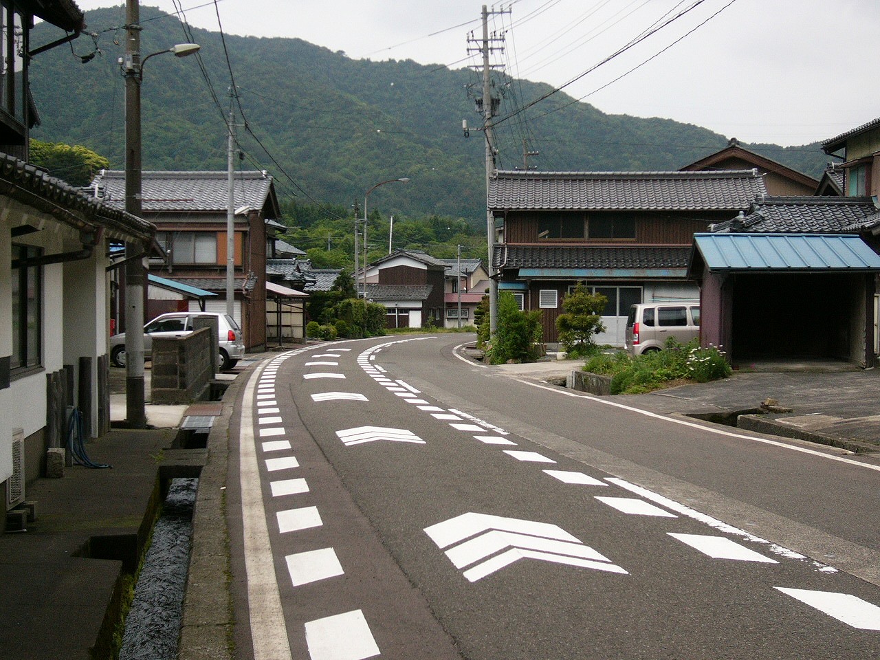 こげ茶の壁の田舎風の家が両脇に並んだ、人一人いない2車線道路