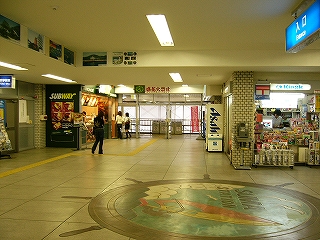 クリーム色のタイルを敷き詰めたコンコース内。少し向こうに二件の店が見える。