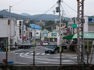 フェンス越しに見る商店の並んだ駅前。