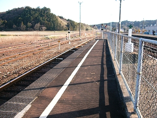 アスファルトの細いホームに白線が伸びる。右脇に低いフェンス。