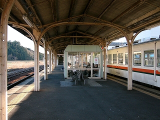 ホームの中央より右寄りに作られたボックス式の待合室のあるホームの風景。上屋を支える古びたクリーム色の鉄骨が良く目立つ。