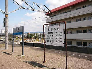 ホームに立つ駅名標、名所案内、背後にマンション。