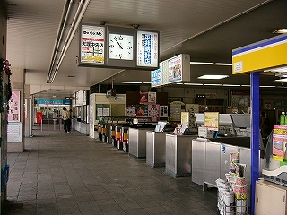 右斜めに見た自動改札の並び。手前の方に有人ブース。売店、天井に設置された時計。