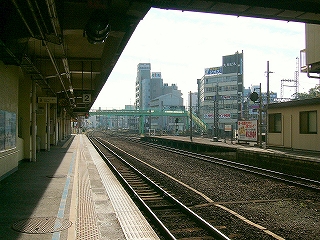 左手に片面ホームの2番線の平らな屋根、右手遠くに、中規模ビルがいくつか立ち並ぶ。