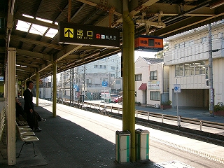 上屋から吊られた紺色とオレンジ色を使った号車案内。駅の裏の風景が見えていて、駐車場や個人ビルなどが並ぶ。