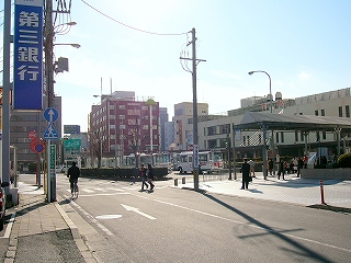 駅前のロータリーの横に入る道路から、駅前を見渡して。右奥に駅舎。