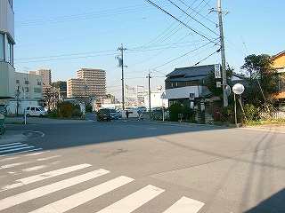 信号も人通りも少ない日陰の大きなＴ字路。Ｔ字路前には人家が二件。ずっと遠くに工場施設が見える。