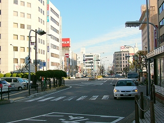 正面に太い大きな道路、遠くに所々6階建てぐらいのビルが見える。