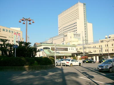 左に植え込みでこんもりしたロータリーの真中の部分、右奥に橋上駅、さらに向こうにはアスト津の高層ビル。