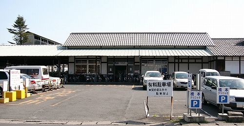 駅舎正面遠景。軒屋根の下に自転車が多くとまっているのが見える。駅前は雑多な様相。