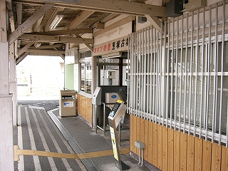 縦の柵が入った窓、その下は薄茶色の壁。その奥に改札機器の並ぶ改札口。