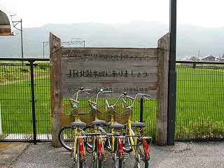 丸太と板でできた案内板のような看板に黒い字で「JR北陸本線に乗りましょう」と書かれている。