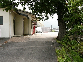 左手に背の高い木々が植割っている狭いスペース、右手に平屋の駅舎。