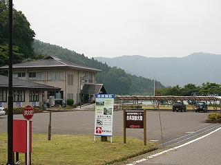 手前に余呉湖観光館の看板、その奥にアスファルトの敷地、左手の方に建物。四角錐の屋根の二階建ての建物。