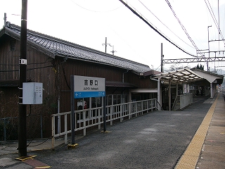 焦げ茶の壁の駅舎の一部とホームとホームに立つ駅名標。